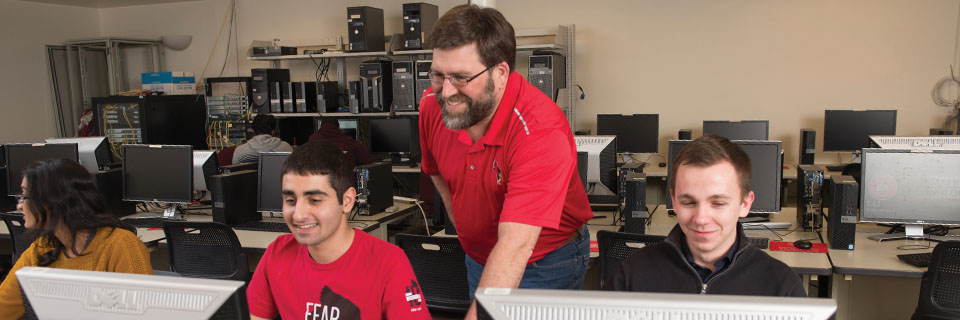 Three students working in a computer lab with their instructor