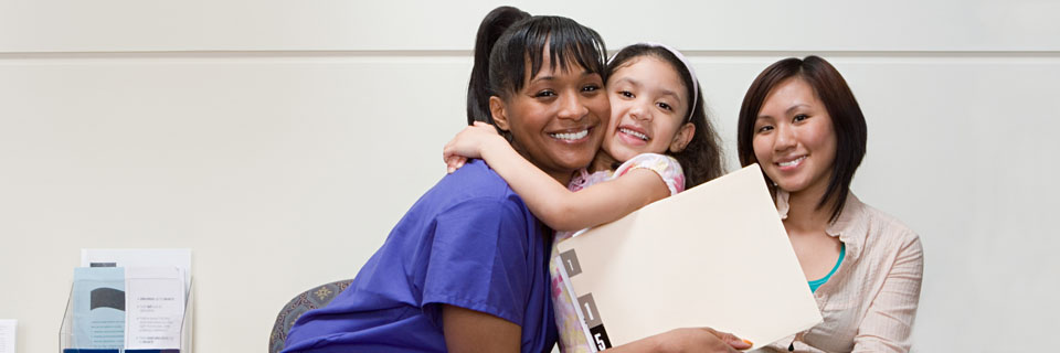 Student nurse embracing in a hug with a little girl and mother sitting next to her.
